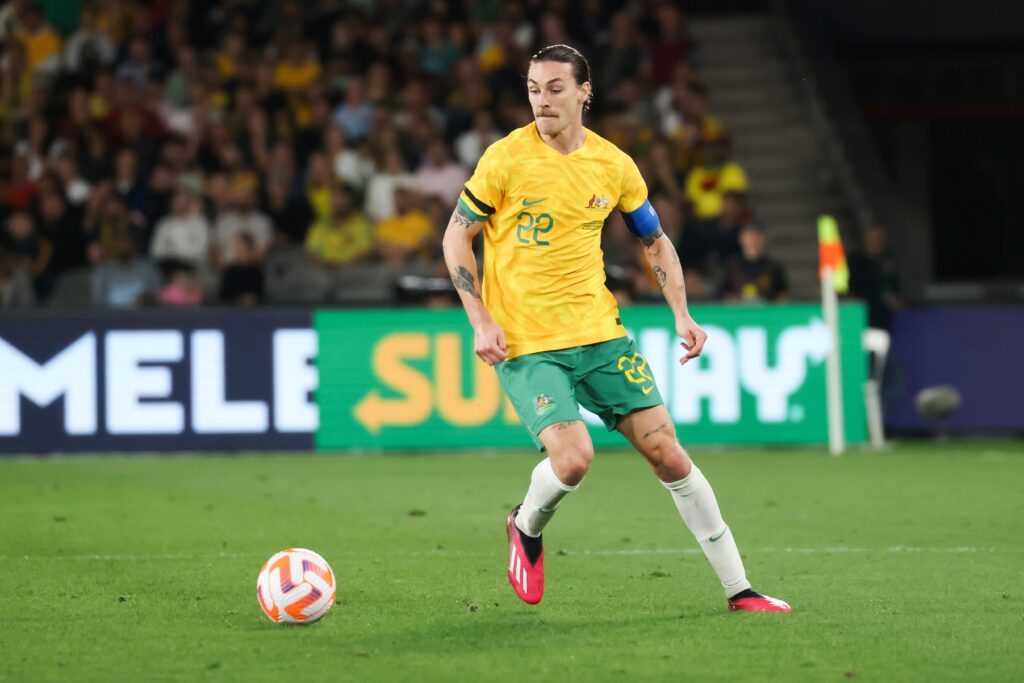 Jackson Irvine, futbolista australiano, conduce el balón durante un partido internacional con la camiseta amarilla de la selección de Australia.