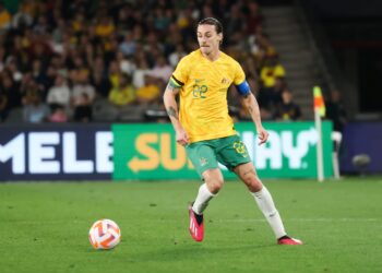 Jackson Irvine, futbolista australiano, conduce el balón durante un partido internacional con la camiseta amarilla de la selección de Australia.