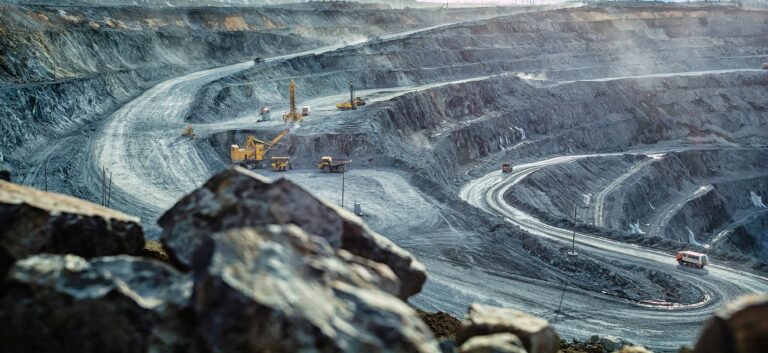 Vista panorámica de una mina a cielo abierto con maquinaria pesada y caminos en espiral, utilizada para extracción de minerales.