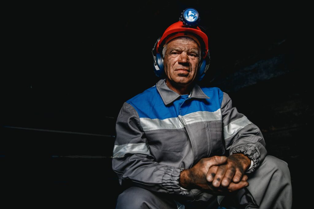 Trabajador del sector minero con casco, lámpara frontal y uniforme de seguridad, con manos cubiertas de polvo tras una jornada laboral.