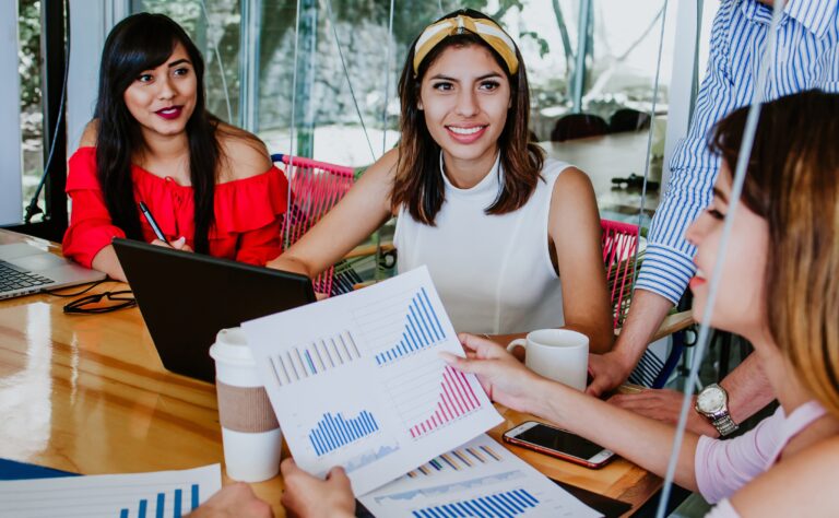 Grupo de mujeres en una reunión revisando gráficos y estadísticas impresas, reflejando la participación femenina en espacios de liderazgo y toma de decisiones laborales.