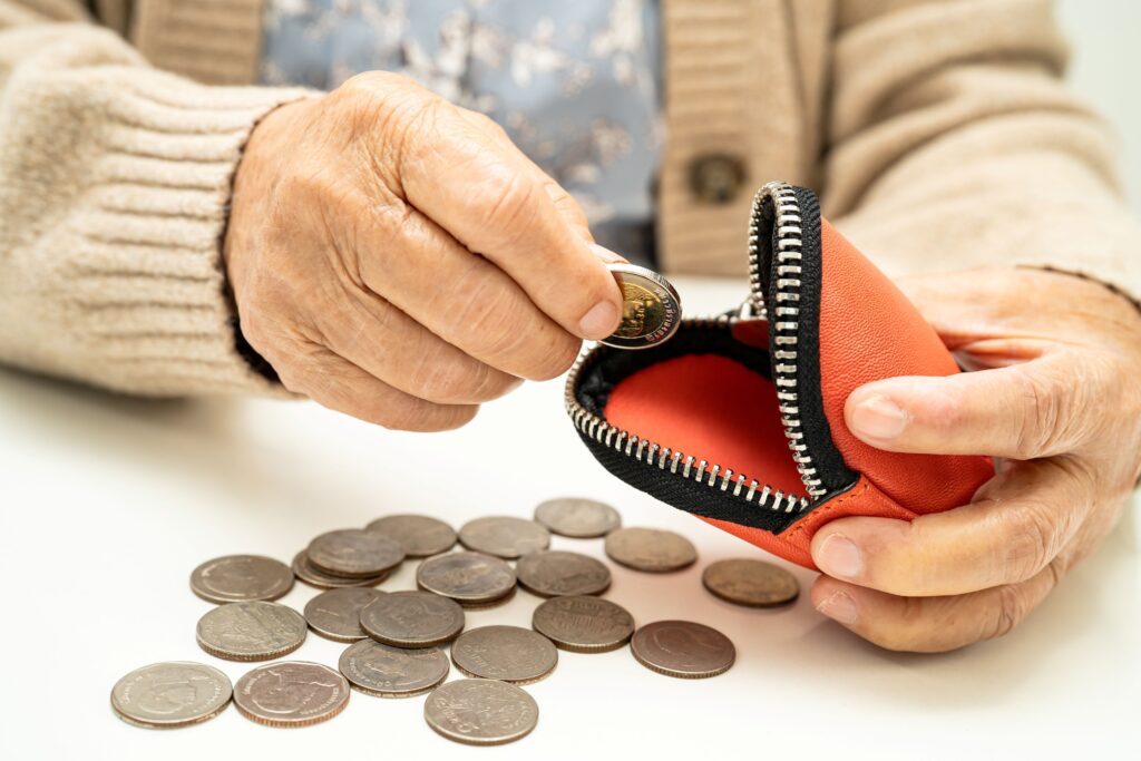 Manos de una persona jubilada contando monedas frente a una cartera, reflejando la espera por el pago de seguros de vida pendientes y la vulnerabilidad económica de los jubilados.