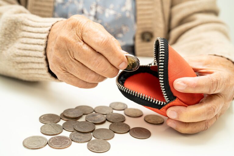 Manos de una persona jubilada contando monedas frente a una cartera, reflejando la espera por el pago de seguros de vida pendientes y la vulnerabilidad económica de los jubilados.