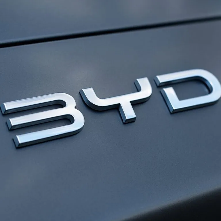 Fotografía del logo de BYD en un automóvil, con acabado metálico y estilo profesional, destacando su identidad visual global