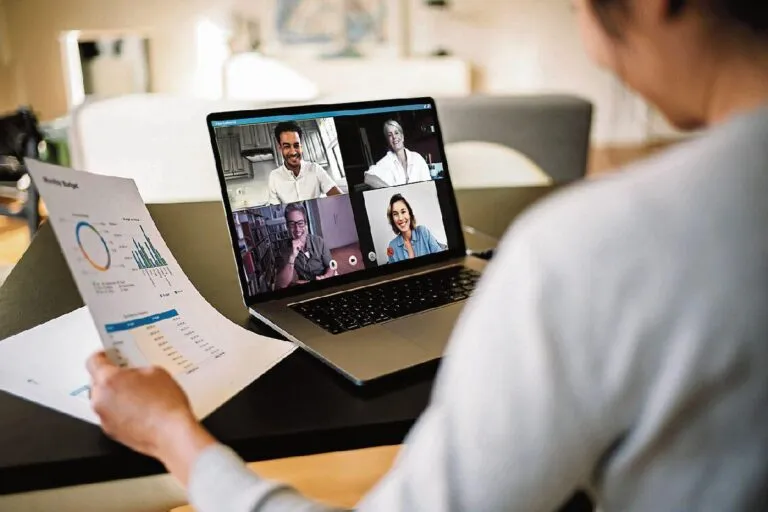 Equipo profesional trabajando en modalidad de trabajo remoto con videollamada y laptops en entorno doméstico organizado